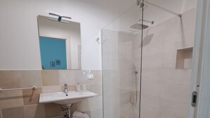 A modern bathroom with a glass-enclosed shower, a white sink, and a wooden shelf. - The scent of calicanto (Tresnuraghes)