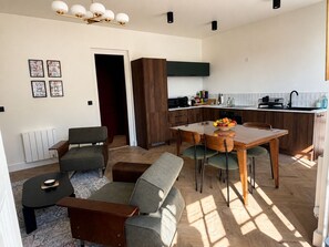 A modern living room with a dining area, a kitchen with wooden cabinets, and a radiator. - Belle Époque Villa - La Batelière - Bow Window - Ocean View - Exceptional (Mers-les-Bains)