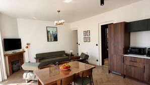 A modern living room with a wooden dining table, a sofa, a television, and a kitchen area with wooden cabinets. - Belle Époque Villa - La Batelière - Bow Window - Ocean View - Exceptional (Mers-les-Bains)