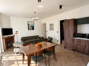 A modern living room with a wooden dining table, a sofa, a television, and a kitchen area with wooden cabinets. - Belle Époque Villa - La Batelière - Bow Window - Ocean View - Exceptional (Mers-les-Bains)