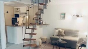 Una scala conduce a una zona cucina, un soggiorno con un divano e un tavolino, e un lampadario a parete.