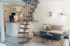 A staircase leading to a kitchen area, a living room with a sofa and a small table, and a wall-mounted light fixture. - Le Clos du Dan, a vacation rental near tourist attractions (Périers-sur-le-Dan)