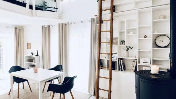 Un soggiorno moderno con un tavolo bianco, sedie nere, una scala in legno e un piano cottura nero.