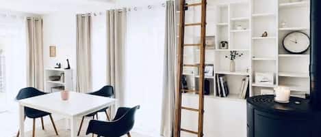 A modern living room with a white table, black chairs, a wooden ladder, and a black stove.
