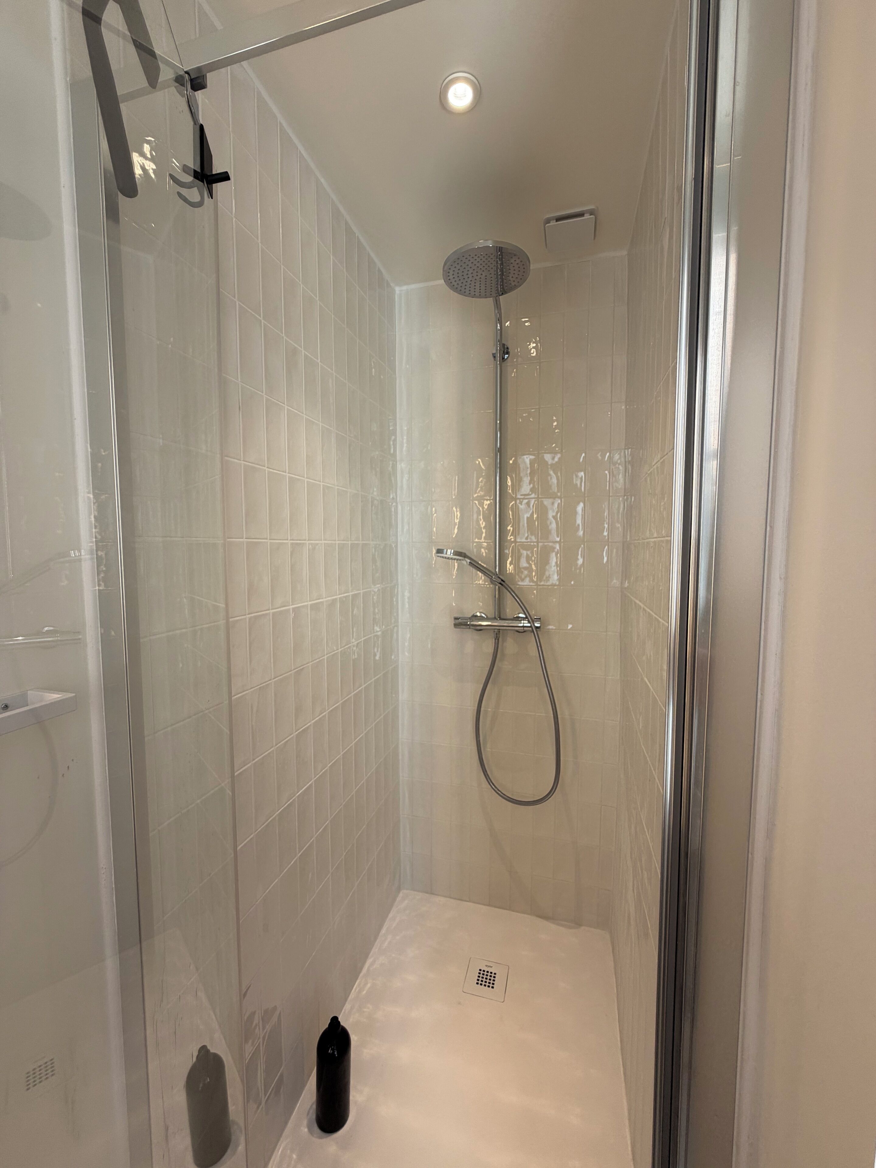 Une douche fermée par des parois en verre, dotée d’un pommeau de douche à main, d’un robinet mural et d’un drain au sol.