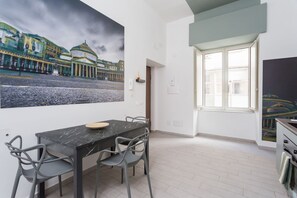 A dining area with a marble table and chairs, a large cityscape painting on the wall, and a window with a view of buildings. - Historic Center Suite By Dimorra  (Naples)
