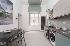 A compact kitchen with a washing machine, a dining area with a table and chairs, and a large window. - Historic Center Suite By Dimorra  (Naples)