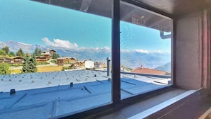 Ein Fenster mit Blick auf eine Wohngegend, einen klaren Himmel und ein Gebirge in der Ferne.