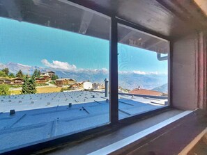 Ein Fenster mit Blick auf eine Wohngegend, einen klaren Himmel und ein Gebirge in der Ferne.