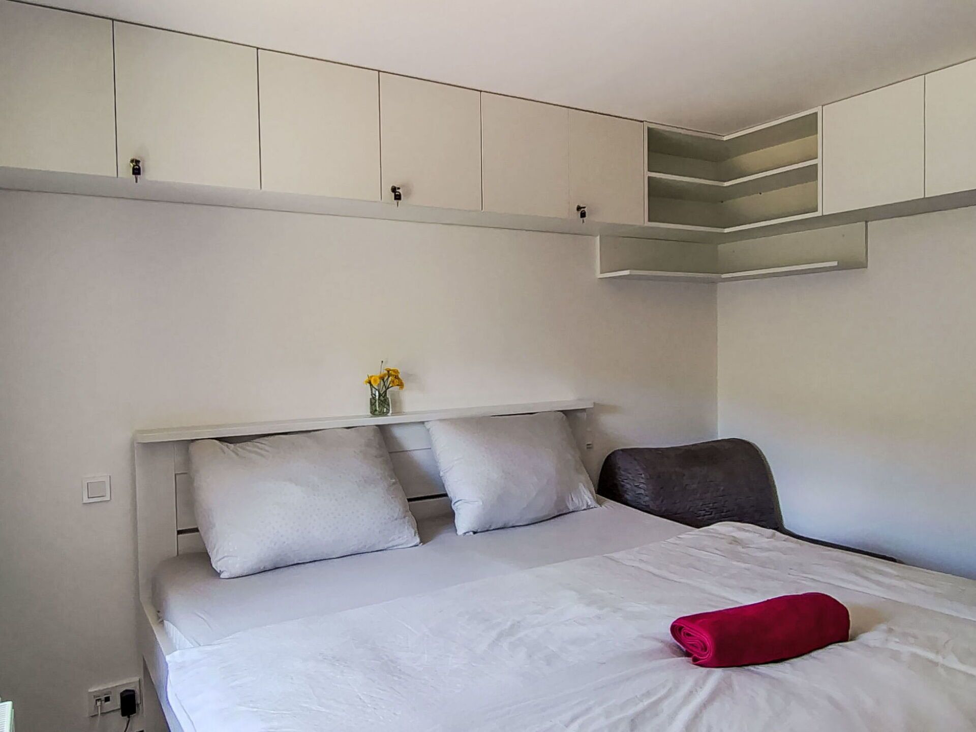 Ein Schlafzimmer mit Bett, Kissen, einem kleinen Tisch mit einer Vase und eingebauten Stauraumschränken.
