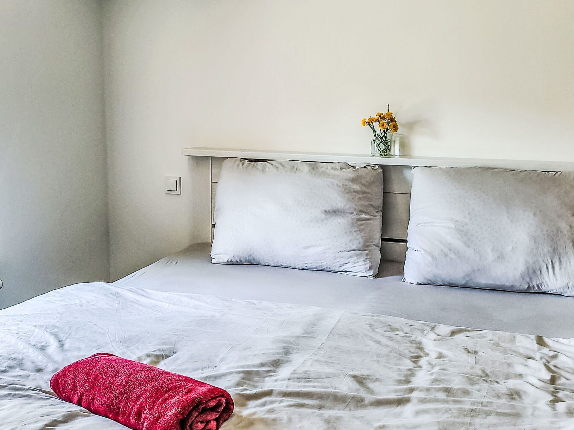 Une chambre à coucher avec un lit, des oreillers, une table de chevet et un vase rempli de fleurs.