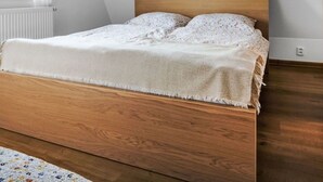 Ein Schlafzimmer mit einem hölzernen Bett, schrägen Deckenbalken, einem weißen Heizkörper und einem Fenster mit Vorhängen.