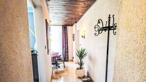 Un couloir avec un plafond en bois, une plante en pot, un luminaire fixé au mur et, au fond, un coin repas.