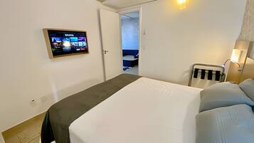 Una habitación de hotel con cama, televisor montado en la pared, mesita de noche con lámpara y puerta que da a un baño.
