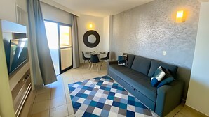 Een moderne woonkamer met een bank, een televisie, een eethoek met stoelen en een kamerbreed tapijt met een patroon.