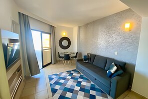 A modern living room with a sofa, a TV, a dining area with chairs, and a patterned rug. - SHB Flat beira-mar no Gonzaga (Santos)