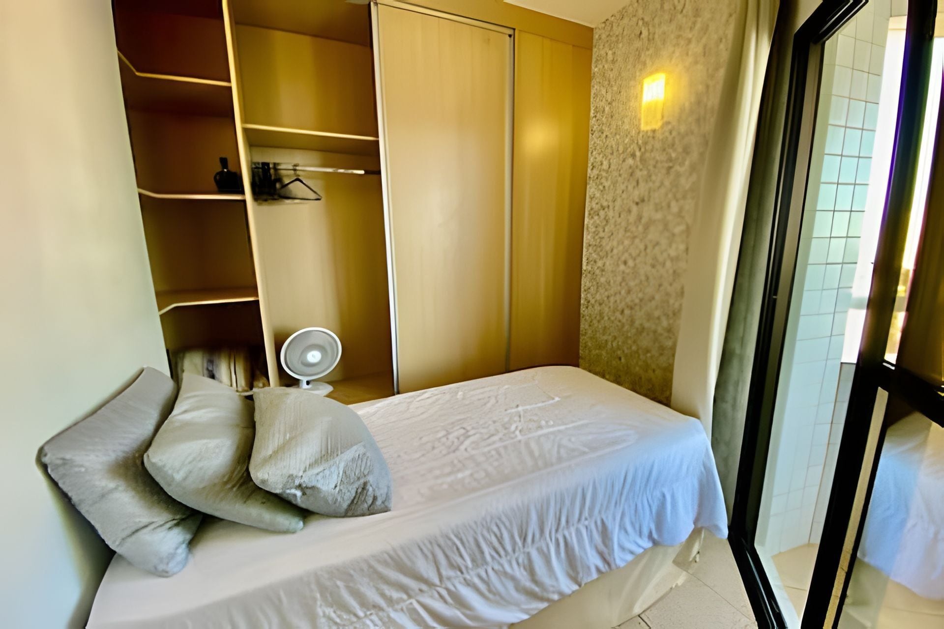 Quarto com cama, almofadas, mesa de cabeceira, espelho e guarda-roupa.