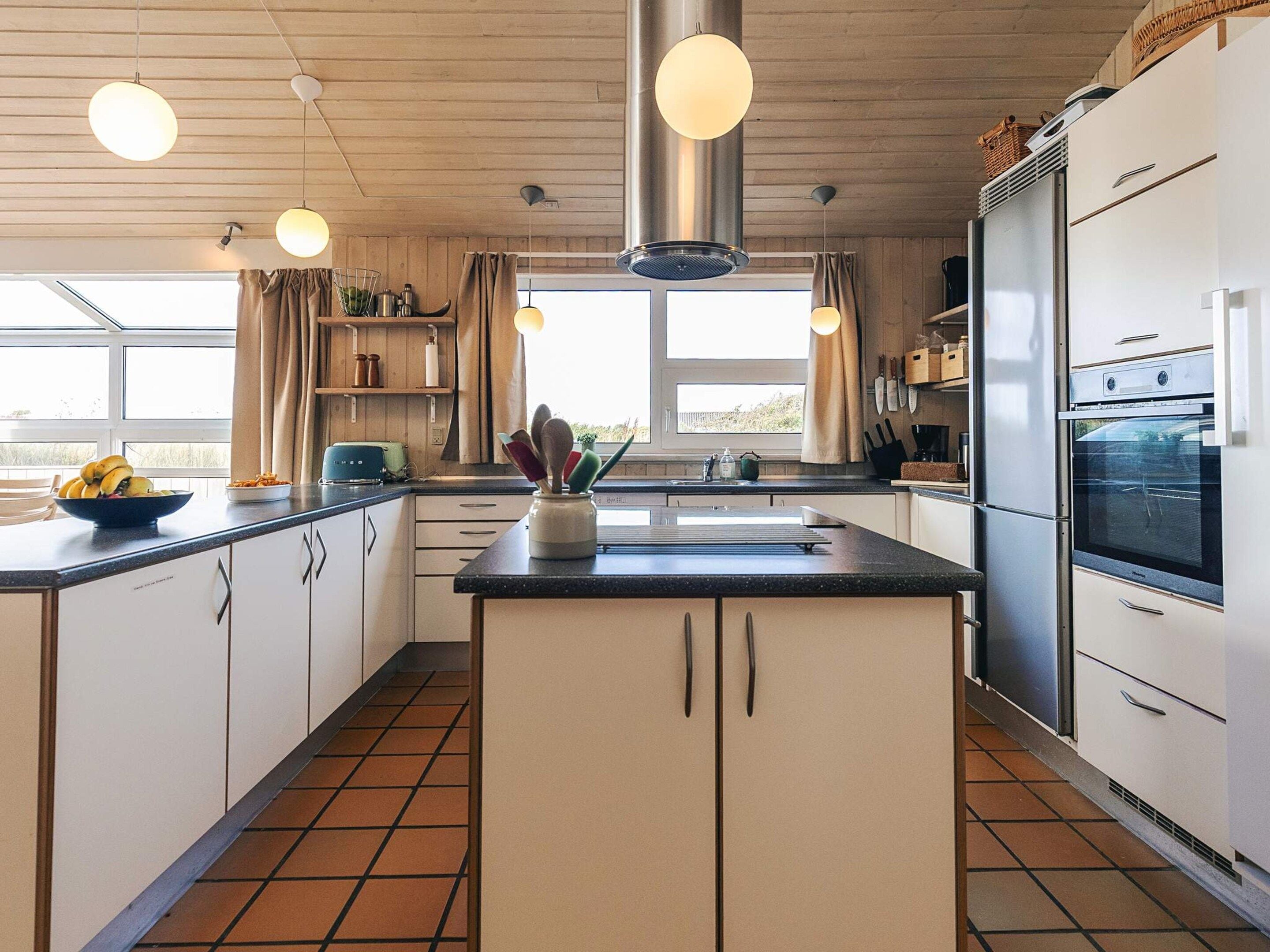 Una cocina moderna con una isla central, electrodomésticos de acero inoxidable e iluminación colgante.