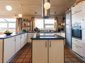 Une cuisine moderne dotée d’un îlot central, d’appareils électroménagers en acier inoxydable et de luminaires suspendus.