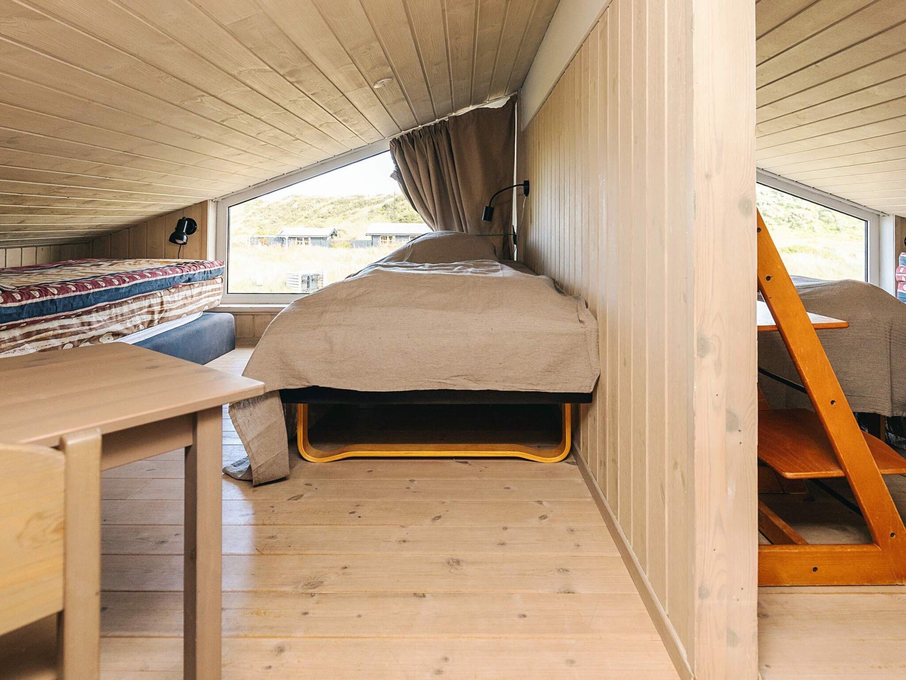 Un intérieur compact, aménagé comme une cabine, avec un lit superposé, une petite table et une fenêtre avec des rideaux.