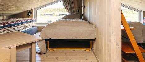 Un intérieur compact, aménagé comme une cabine, avec un lit superposé, une petite table et une fenêtre avec des rideaux.