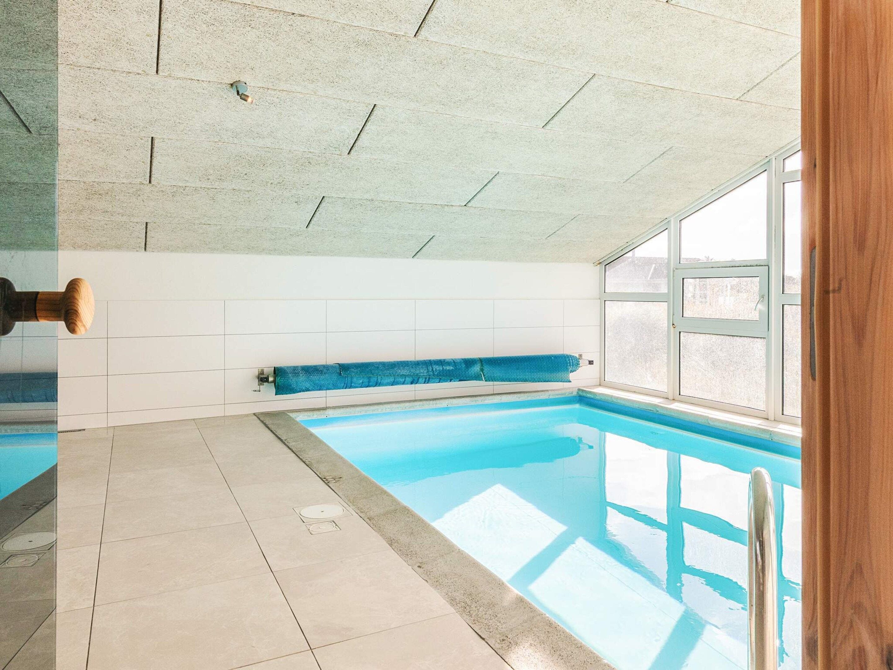 Ein Hallenbad mit gefliestem Boden, einer blauen Poolabdeckung und einem Fenster, das für natürliches Licht sorgt.