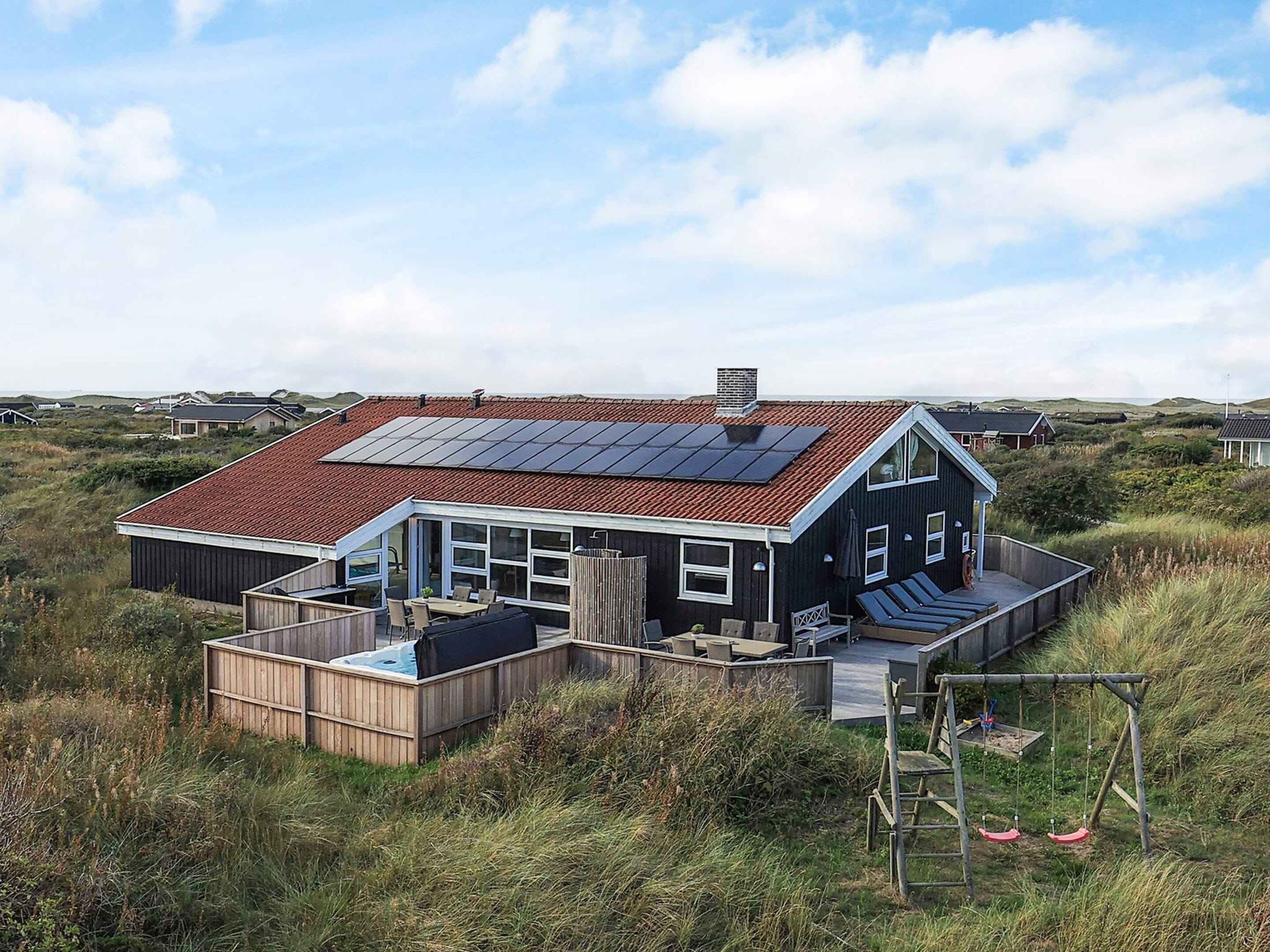 A house with a red roof, solar panels, a wooden deck, and a swing set.