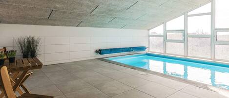 An indoor swimming pool with tiled flooring, a wooden bench, and potted plants.