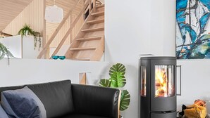 Ein modernes Wohnzimmer mit einem schwarzen Ledersofa, einer Holztreppe, einem schwarzen Kaminofen und einem großen abstrakten Gemälde.
