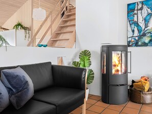 Ein modernes Wohnzimmer mit einem schwarzen Ledersofa, einer Holztreppe, einem schwarzen Kaminofen und einem großen abstrakten Gemälde.