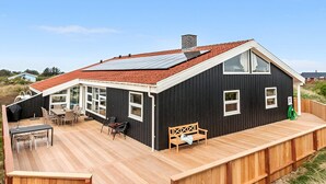 Ein schwarzes Haus mit rotem Dach, einer Holzdiele und einer überdachten Veranda mit Glas.