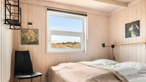 Ein Zimmer mit Bett, Sessel, Fenster mit Blick und Wandlampe.