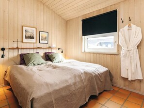 Ein Schlafzimmer mit Bett, Kissen, einem Fenster mit Blick und einem aufgehängten Bademantel sowie Wandbildern.