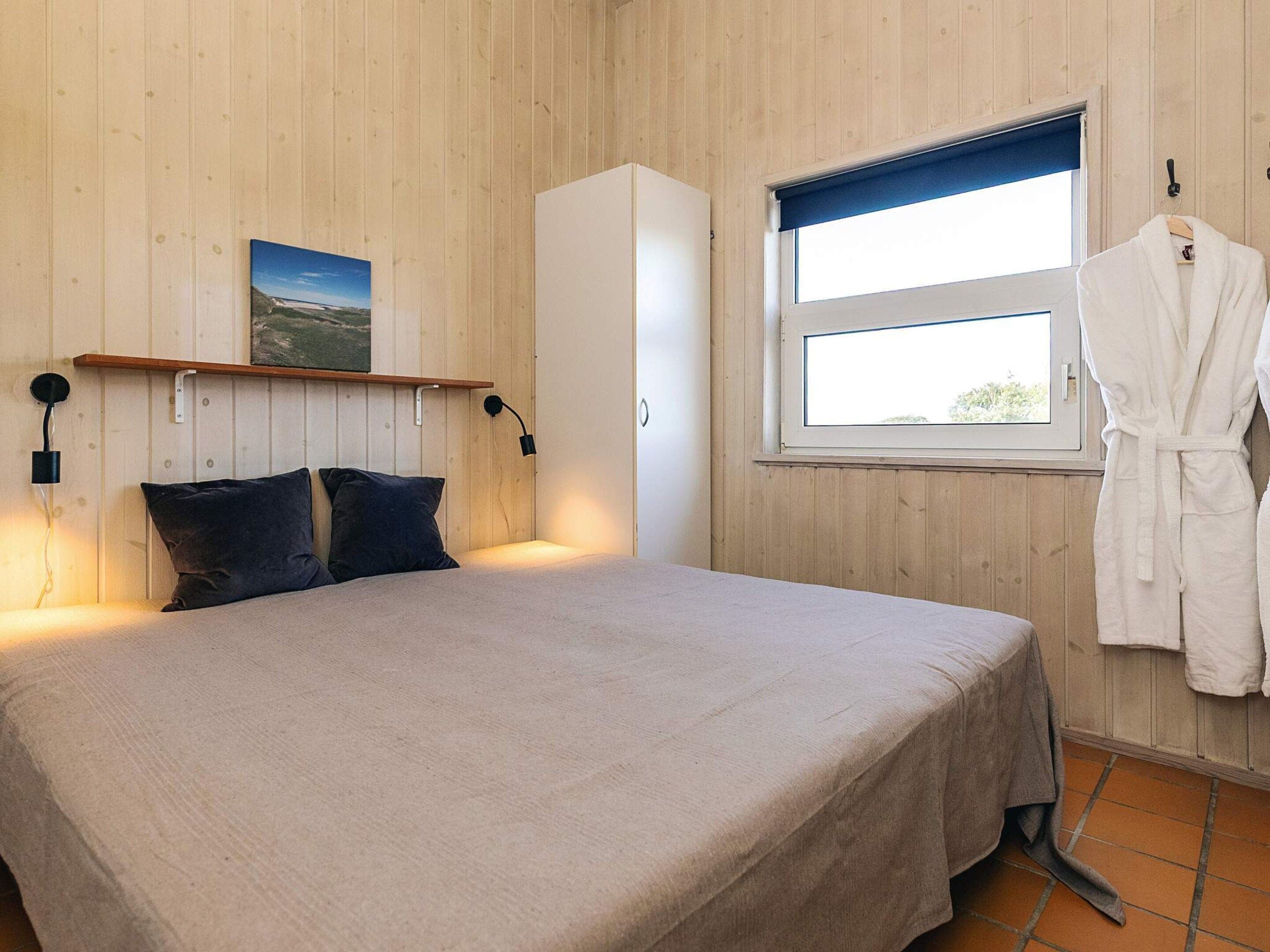 A bedroom with a bed, a wardrobe, a window with a view, and a robe hanging by the window.