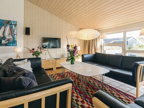 Ein modernes Wohnzimmer mit einer Couch, einem Couchtisch und einem Fernseher. Auf dem Tisch stehen Blumen und an der Wand hängt ein Gemälde.