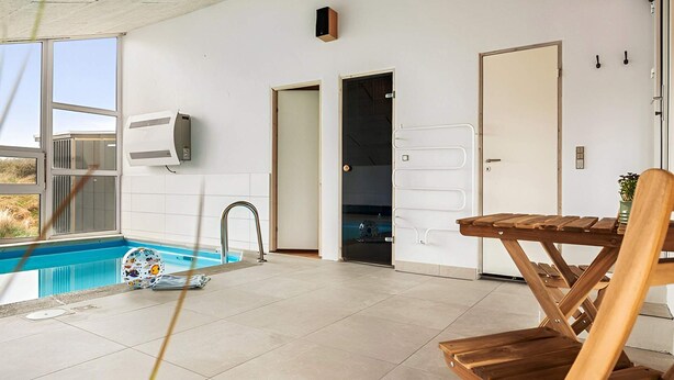 Ein moderner Innenbereich mit Schwimmbad, einem Holztisch und -stühlen, einer Tür und einem Fenster.