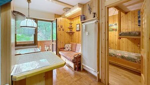 Ein gemütliches Blockhauss-Interieur mit Holztisch, Bank, Heizkörper und einem Fenster mit Blick ins Grüne.