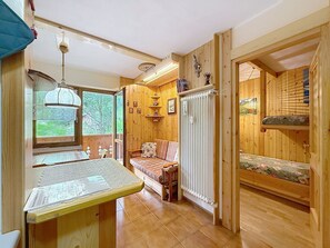 Ein gemütliches Blockhauss-Interieur mit Holztisch, Bank, Heizkörper und einem Fenster mit Blick ins Grüne.
