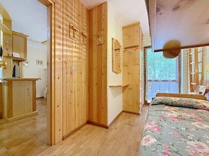 Ein Zimmer mit Holzwänden, einem Bett mit floralem Bettzeug, einem Schreibtisch mit Computer und einem Fenster mit Blick auf Bäume.