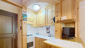 Eine kleine Küche mit Holzschränken, einem Gasherd, einer Spüle und einem Fernseher.