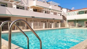 Una piscina amb baranes metàl·liques, una zona coberta amb gandules i un edifici d'estil arquitectònic modern.