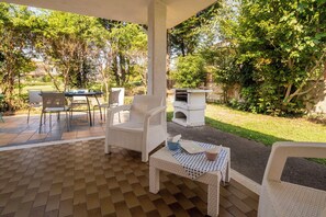 An outdoor patio with a checkered floor, white wicker furniture, and a barbecue grill.