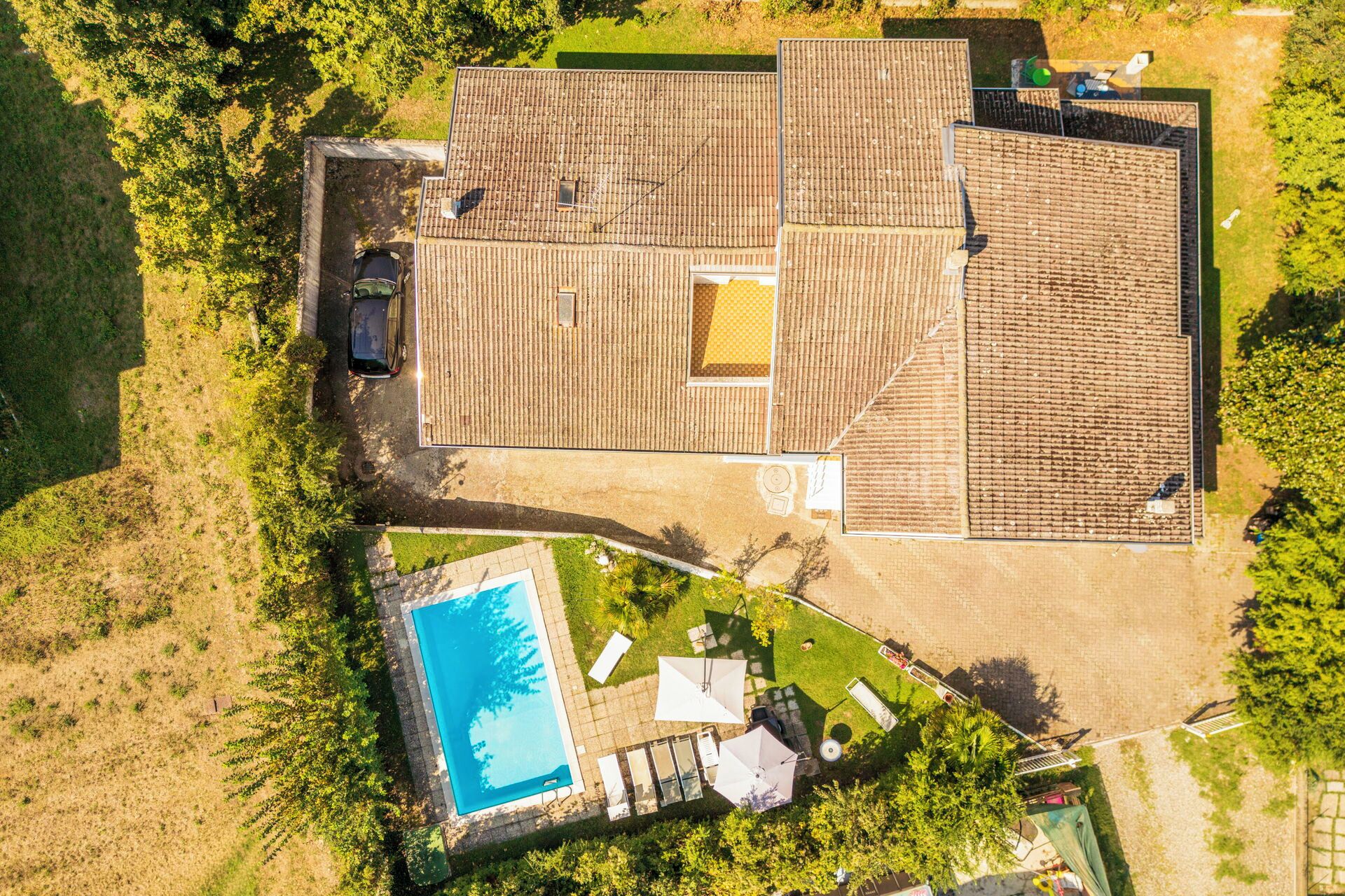 Vista aérea de una propiedad con piscina, patio cubierto y un coche estacionado afuera.