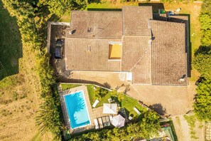 An aerial view of a property with a swimming pool, a covered patio, and a car parked outside.