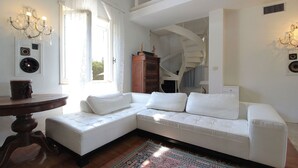 Ein weißes Ecksofa, ein runder Holztisch, ein gemustertes Teppich und eine Wendeltreppe.