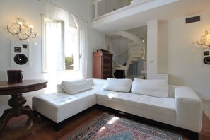 Ein weißes Ecksofa, ein runder Holztisch, ein gemustertes Teppich und eine Wendeltreppe.