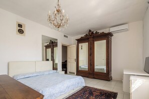 A bedroom with a bed, a wooden wardrobe, a chandelier, and a small desk.