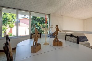 A room with a white table, two wooden sculptures, a candelabra, and a view of greenery outside.