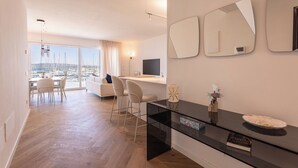 Moderni olohuone, jossa on ruokailutila, televisio ja suuri ikkuna, josta avautuu näkymä venesatamaan.