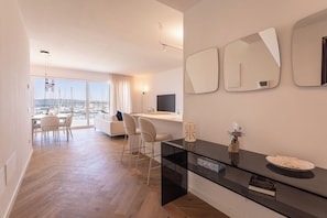Ein modernes Wohnzimmer mit Essbereich, Fernseher und großem Fenster mit Blick auf einen Jachthafen.